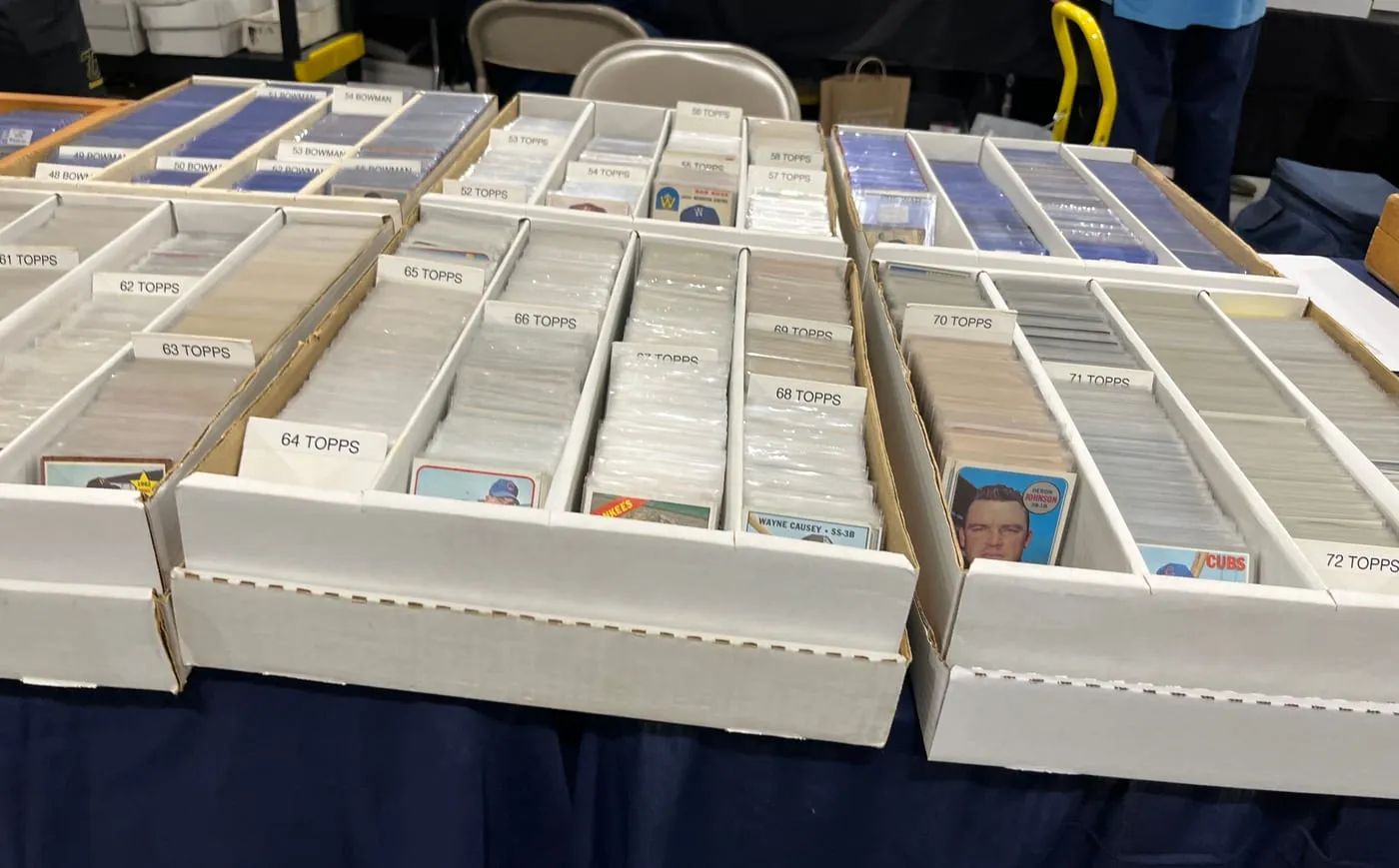 Rows of vintage baseball cards sorted by year at a card show — 1950s Bowman and 1960s–70s Topps