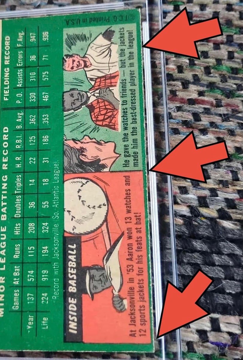 The back of a 1954 Topps Hank Aaron card in a plastic holder, photographed sideways so the right edge runs down the frame. Three arrows point at that edge, where the green cardboard shows a fibrous, frayed line along the cut.